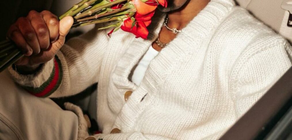 joe boy smelling roses in a car wearing white